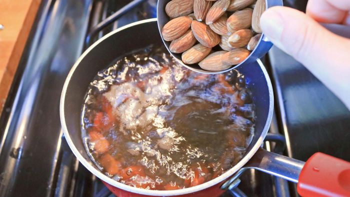 Almonds being poured into boiling water in a pot.