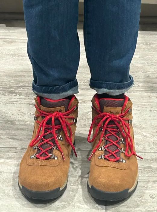 A person rocking rolled-up jeans and tan hiking boots with vibrant red laces.
