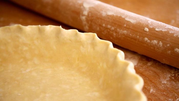 A pie crust resting next to a rolling pin.