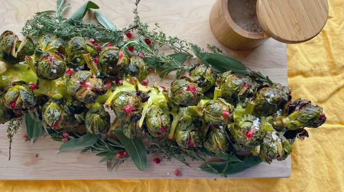 A full stalk of roasted Brussels sprouts displayed on a cutting board.