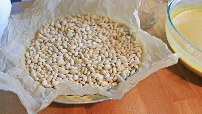 A pie crust lined with parchment paper and filled with baking beans.