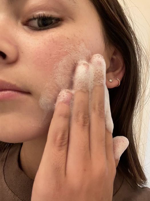 A reviewer gently massaging a foamy cleanser into their cheek.
