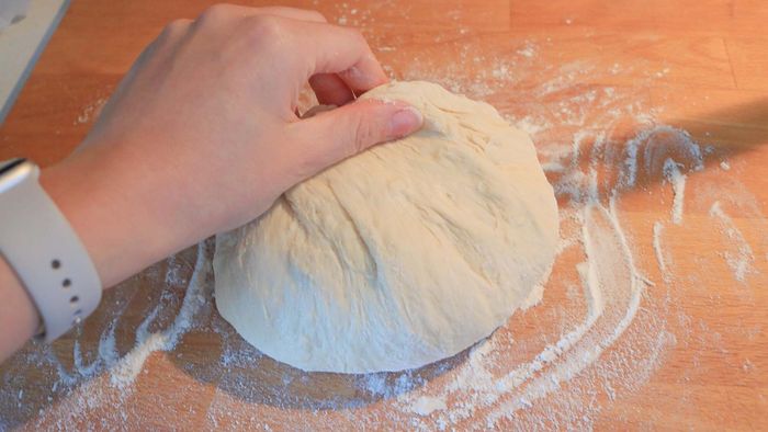 A hand picking up a ball of dough from a countertop.