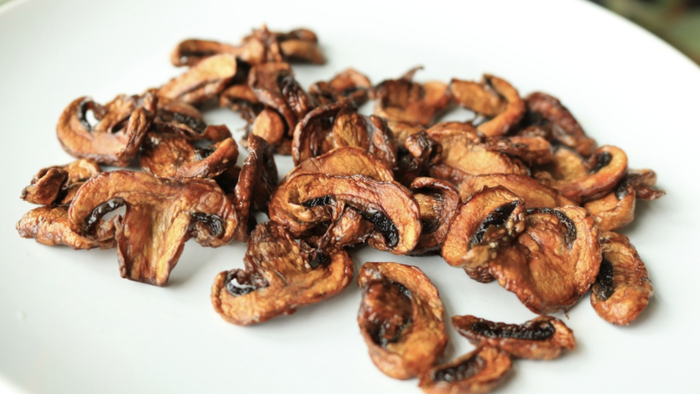 Golden air-fried mushroom slices arranged neatly on a white plate.