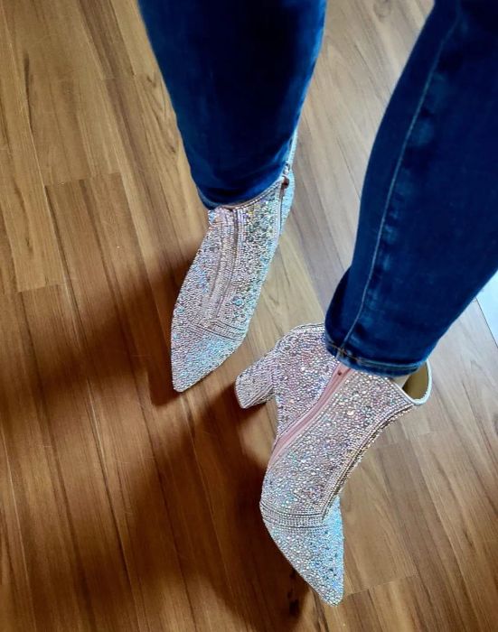 A reviewer shows off the rhinestone-covered boots paired with blue jeans for a chic, glitzy look.