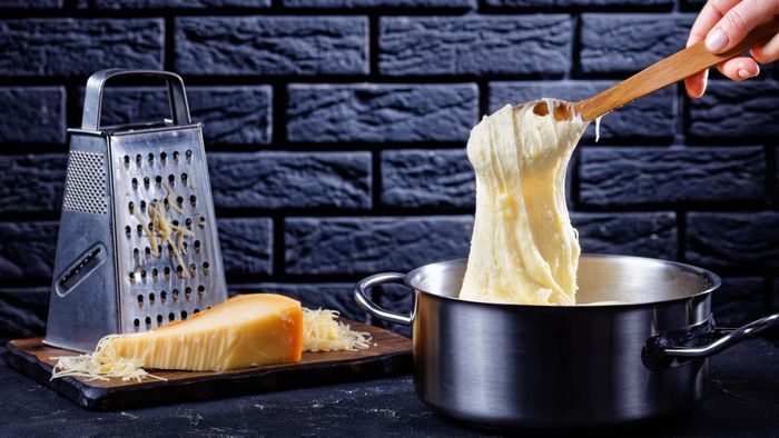 A pot of pommes aligot placed beside a box grater and cheese.