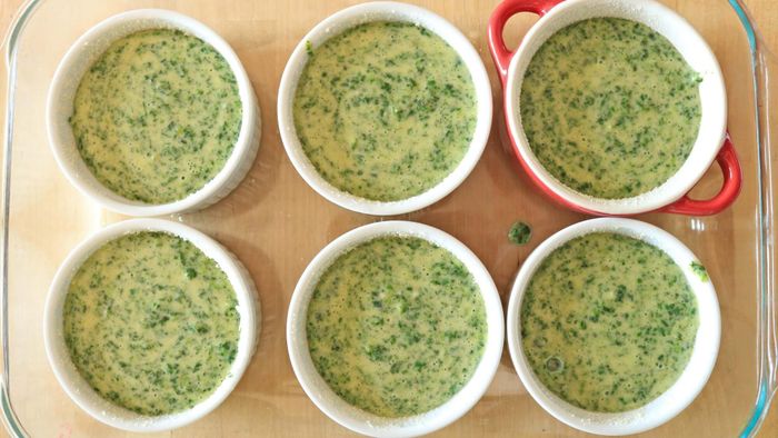 Ramekins placed in a casserole dish, filled with spinach batter.