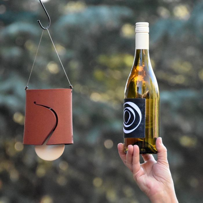 A hand gripping a wine bottle with a distinctive label, placed next to a stylish leather wine holder hanging nearby