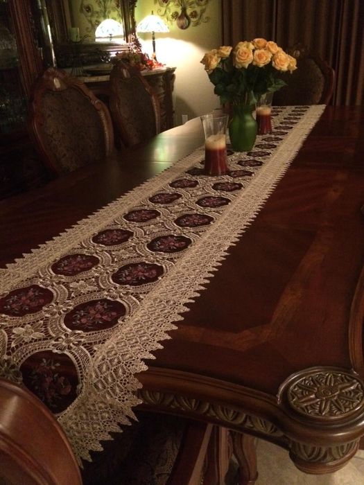An exquisite dining table adorned with a detailed table runner and a beautiful bouquet of roses in a vase.