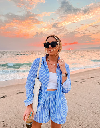 A reviewer sports an oversized blue and white striped button-up top, paired with matching high-waisted elastic shorts.