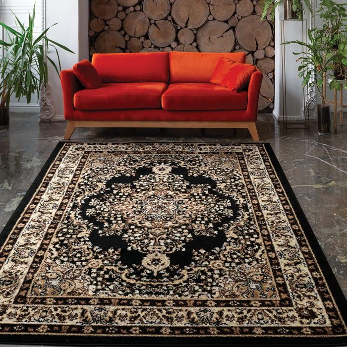 A traditional black and beige area rug placed on the floor, with a red couch resting behind it.
