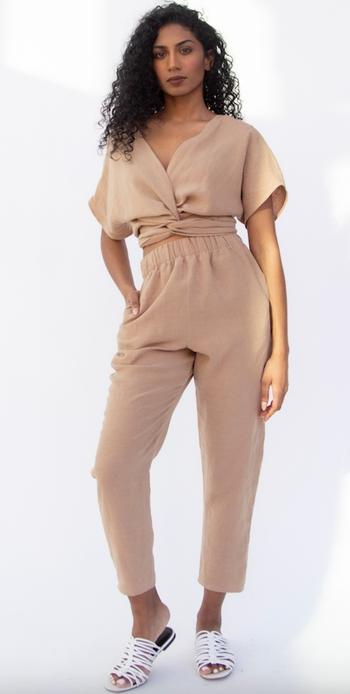 A woman in a casual beige top and linen pants paired with white sandals.