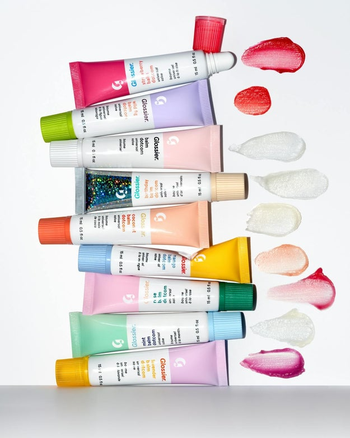 A collection of Glossier lip balm tubes in various shades, with product swatches on a clean white background