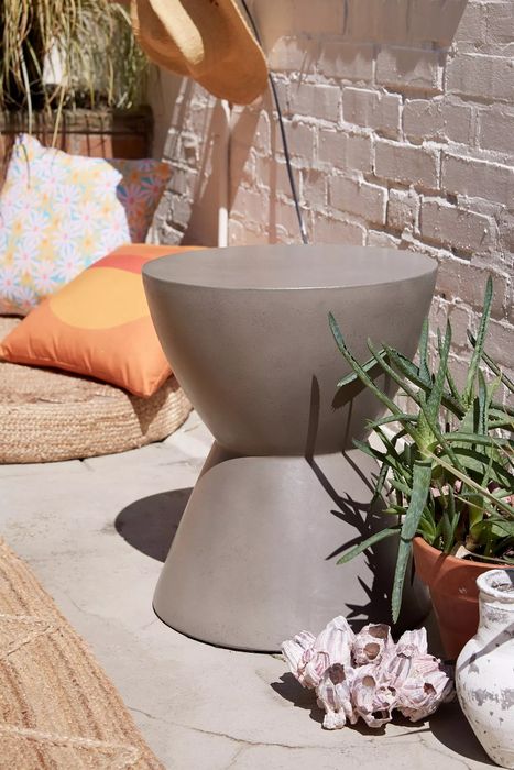 A concrete side table set in an outdoor space, complemented by plants and decorative accents nearby