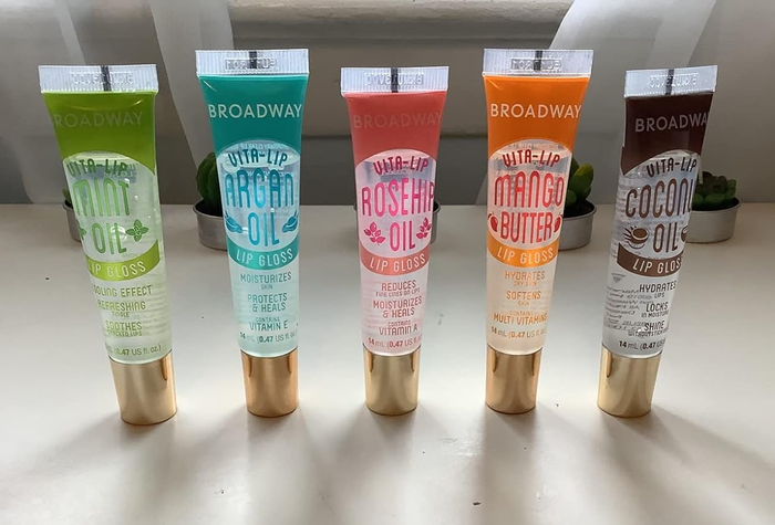 Five different tubes of Broadway Vita-Lip lip gloss, showcasing various flavors such as mint oil, argan oil, rosehip oil, mango butter, and coconut oil, neatly arranged on a shelf