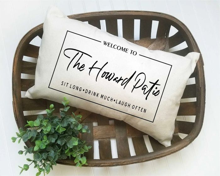 A white rectangular cushion nestled inside a brown wicker basket with the inscription,