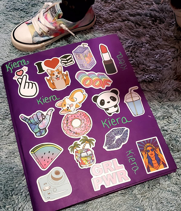 A purple notebook adorned with a variety of vibrant stickers, including animals, a camera, and phrases like 