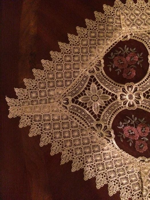 A lace tablecloth featuring delicate floral patterns, elegantly draped over a wooden surface.