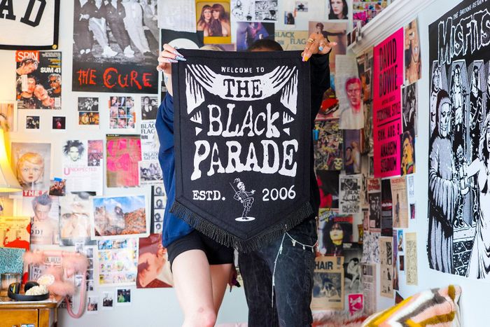 Two people proudly holding up a banner in front of a bedroom wall covered in magazines.