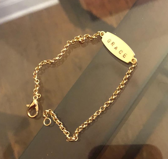 A gold bracelet featuring the engraved word 'Grace'.