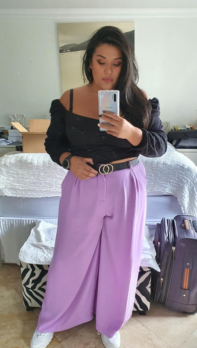 A reviewer taking a mirror selfie dressed in a puff-sleeve top and wide-leg trousers, accessorized with a belt.