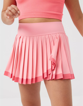 A model rocking a pleated tennis skirt and a pink crop top, captured in a midsection view.