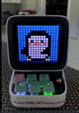 A compact speaker with a screen displaying a dancing penguin pixel graphic and a small keyboard featuring six keys.