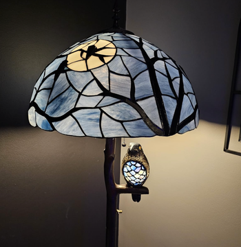 A Tiffany-style lamp with a base resembling a tree trunk, topped with a stained-glass shade depicting a tranquil night sky.