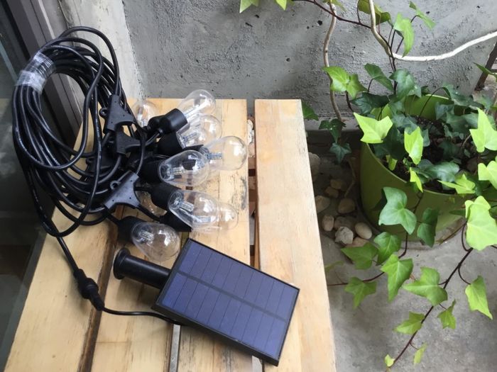 A solar panel beside string lights on a wooden table with a nearby plant.