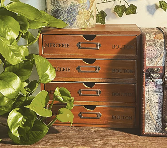 A vintage-style wooden storage cabinet with labeled drawers, placed beside a plant and decorative items, adding a touch of old-world charm.