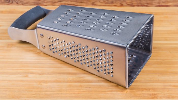 A box grater lying on its side atop a wooden surface.