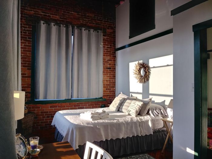 A bright bedroom with a neatly arranged bed, sheer curtains, and exposed brick walls, featuring cozy decor.