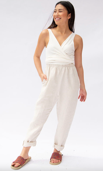 A model in a white top and linen pants, smiling and walking forward.
