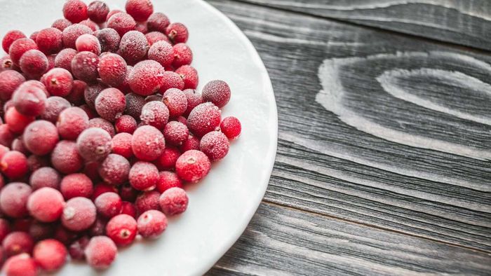 A plate filled with frozen cranberries rests atop a wooden table.