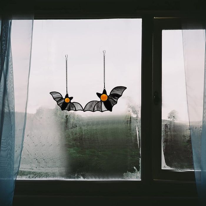 A pair of bat-shaped suncatchers hanging in a window, casting eerie shadows.