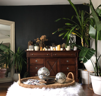 A vintage wooden dresser adorned with plants, candles, and two disco balls, placed in a cozy, inviting room.