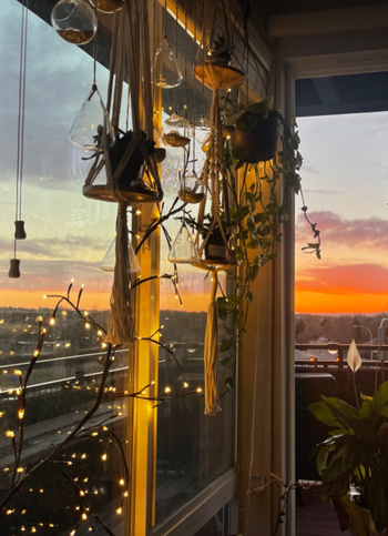 A cozy balcony bathed in sunset light, adorned with hanging plants, string lights, and offering a clear view of the sky — perfect for inspiring home decor ideas