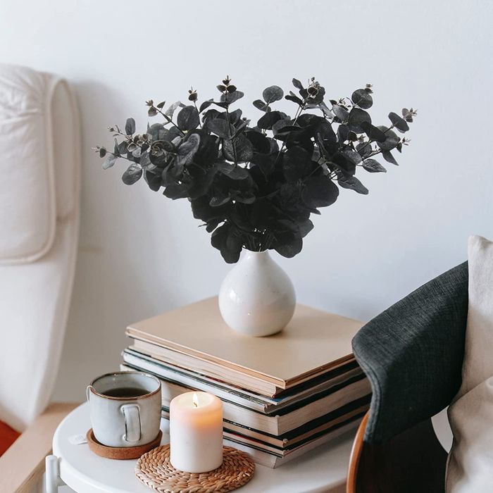 A bundle of black eucalyptus in a vase, resting on a stack of books.