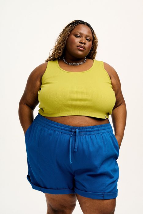 A woman confidently stands in a sleeveless top and shorts with her hands on her hips.