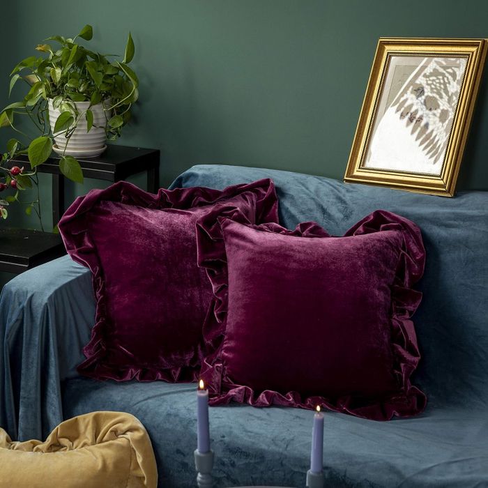 Two luxurious velvet pillows resting on a bed, accompanied by a framed picture and elegant candlesticks, offering a beautiful home decor inspiration.