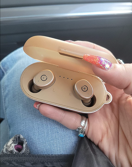 A reviewer holding a pale pink charging case with matching wireless earbuds inside.