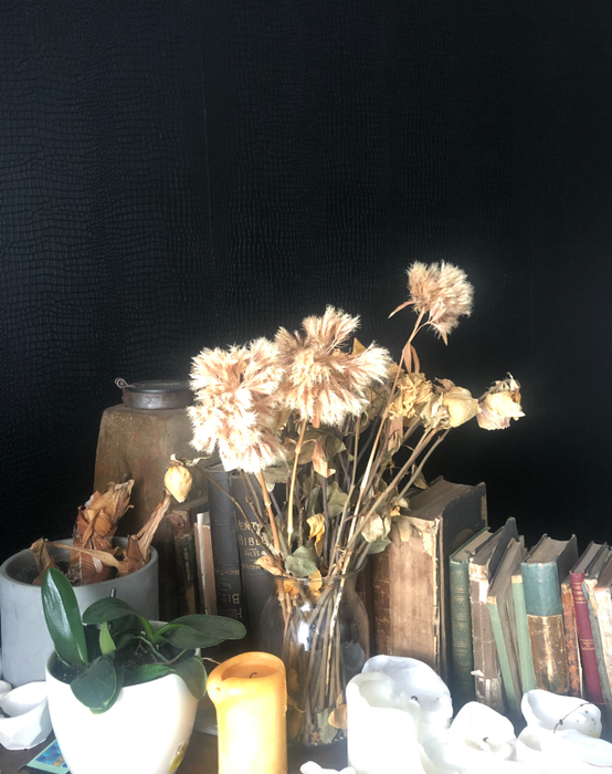 Dried flowers arranged in a vase beside old books and various candles, creating a timeless, vintage vibe.