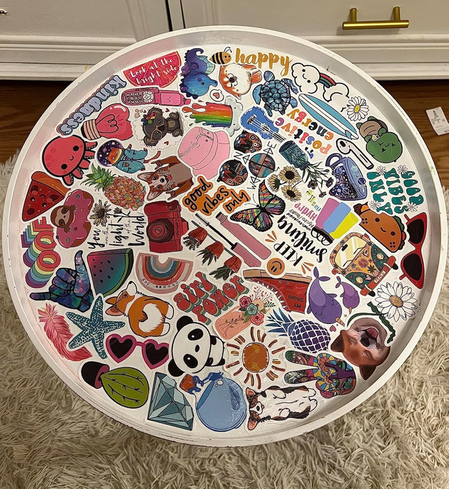 Round tabletop covered with an eclectic mix of stickers featuring flowers, rainbows, and fun designs, resting on a fluffy rug
