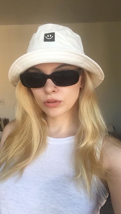 reviewer sporting the same style of sunglasses while wearing a white bucket hat