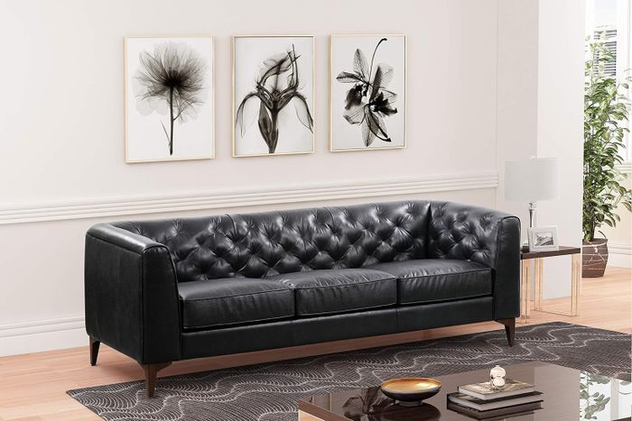 A sleek black tufted leather sofa, beautifully placed in a contemporary living room, complete with stylish wall art and décor. A perfect update to bring a touch of chic elegance into your home.