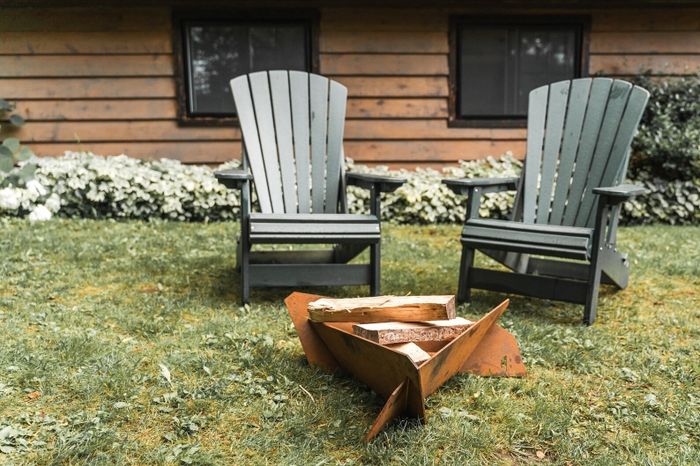 Two wooden Adirondack chairs positioned around a cozy fire pit in a serene backyard setting