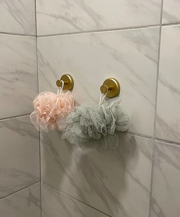Two loofahs hanging from golden hooks against a tiled shower wall.