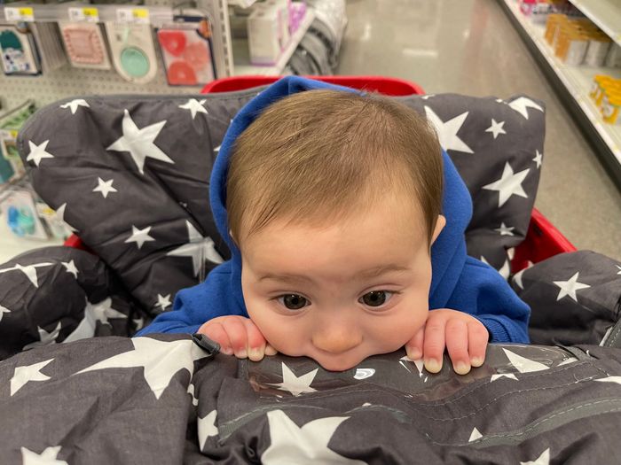 A baby sitting comfortably in a grey shopping cart cover decorated with white stars.