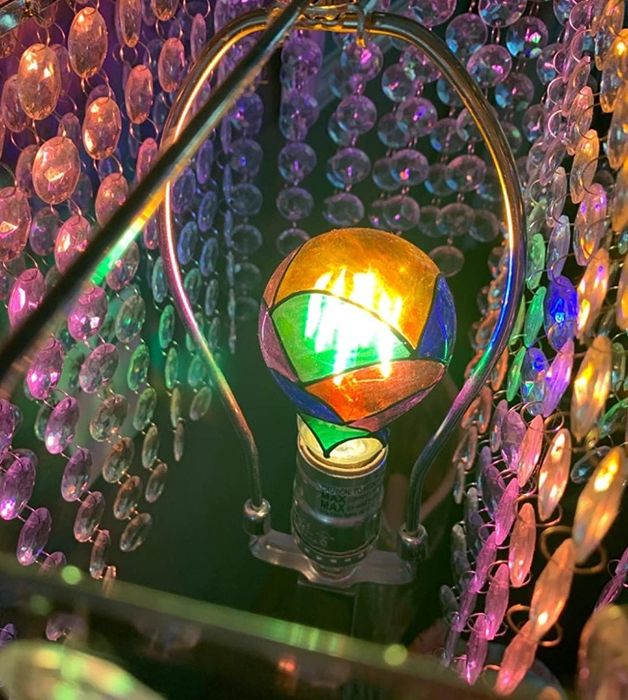 A close-up view of a multicolored, iridescent light bulb nestled within a crystal chandelier.