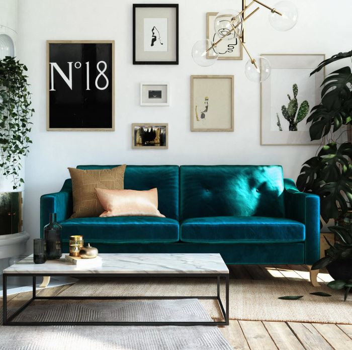A modern living room featuring a plush velvet sofa, a collection of framed artwork on the walls, and thriving indoor plants.